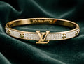 Gold Louis Vuitton stainless steel bracelet on a dark green fabric background
